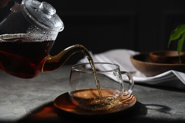 Pouring hot tea into cup on grey table, closeup