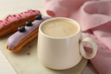 Cup of coffee and delicious eclairs covered with glaze on white wooden table, closeup