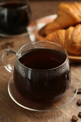 Hot coffee in glass cup and beans on wooden table, closeup