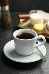 Fototapeta premium Hot coffee in cup, saucer and spoon on dark textured table, closeup
