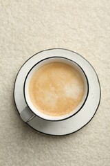 Tasty cappuccino in cup and saucer on light textured table, top view