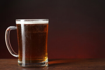 Mug with fresh beer on wooden table against color background. Space for text