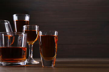 Different delicious liqueurs in glasses on wooden table, space for text