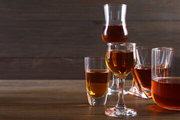 Different delicious liqueurs in glasses on wooden table, space for text