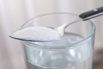 Glass of water and spoon with baking soda on light background, closeup