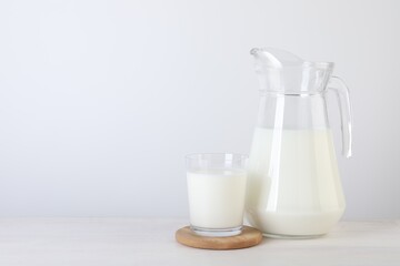 Jug and glass of fresh milk on wooden table, space for text