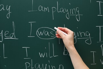 English teacher writing with chalk on green chalkboard, closeup