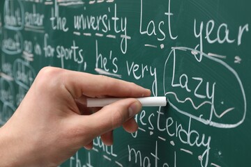 English teacher writing with chalk on green chalkboard, closeup