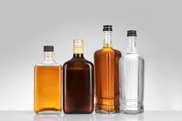 Bottles of different alcoholic drinks on white table against light background