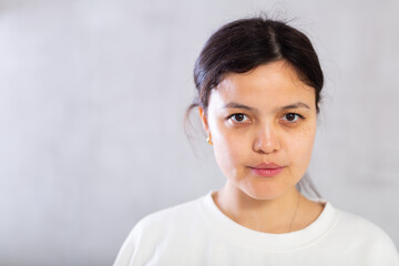 Closeup portrait of focused serious young brunette with hair tied back in bun, looking at camera confidently. Studio photoshoot on gray background