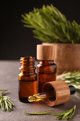 Essential oil in bottles, dropper and rosemary on grey table