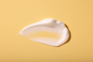 Sample of face cream on pale yellow background, top view