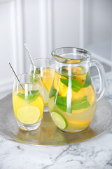 Freshly made lemonade with mint in jug and glasses on white marble table
