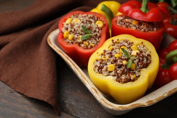 Quinoa stuffed bell peppers and basil in baking dish on wooden table, closeup. Space for text