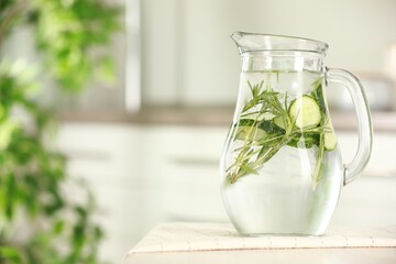 Refreshing cucumber water with rosemary in jug on white table, closeup. Space for text