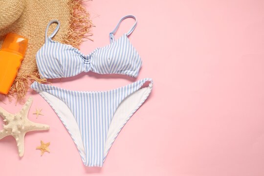 Striped swimsuit, sunscreen, hat and starfishes on pink background, flat lay. Space for text