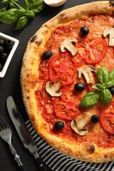 Delicious pizza with tomatoes, mushrooms, olives and basil served on black wooden table, flat lay