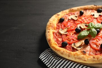 Delicious pizza with tomatoes, mushrooms, olives and basil on black wooden table, closeup