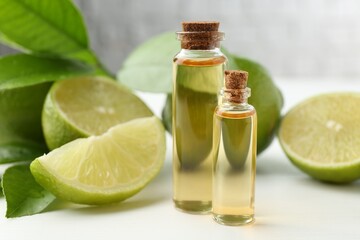 Essential oils in bottles, limes and green leaves on white table, closeup