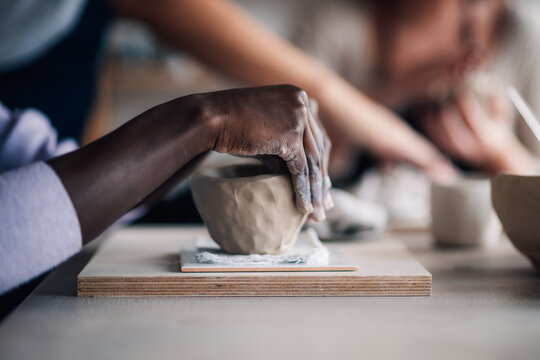Close up of diverse pottery class attendee's hands modeling clay.