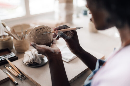 Close up of diverse pottery class attendee decorating clay work at studio