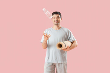 Naklejka premium Sporty young man with bottle of water and fitness mat on pink background