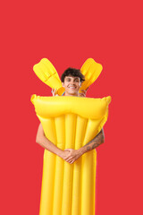 Young man with swim mattress and flippers on red background