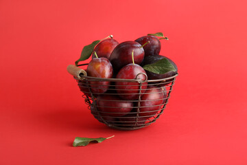 Basket with fresh ripe plums and leaves on red background