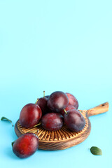 Wooden board with fresh ripe plums on blue background