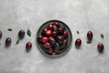 Plate with fresh ripe plums and leaves on grey background