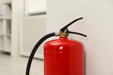 Fire extinguisher near light wall indoors, closeup