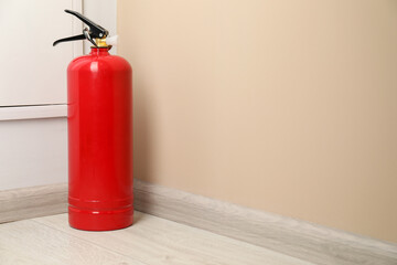 Fire extinguisher on floor near beige wall indoors, space for text
