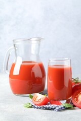 Tasty tomato juice with fresh vegetables and basil leaves on light grey table