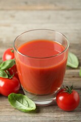 Tasty tomato juice in glass, basil leaves and fresh vegetables on wooden table, closeup
