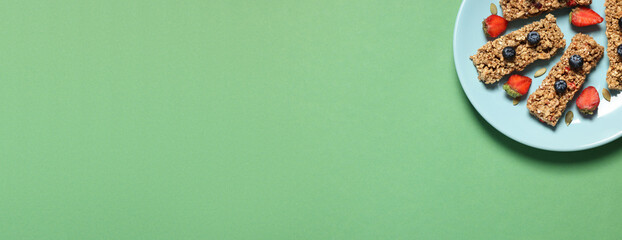 Tasty homemade granola bars and berries on light green table, top view. Banner design with space for text
