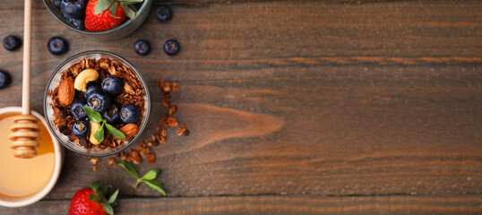 Tasty dessert with granola, yogurt, nuts and berries on wooden table, flat lay. Banner design with space for text