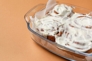 Baking dish of tasty cinnamon rolls with cream on brown background