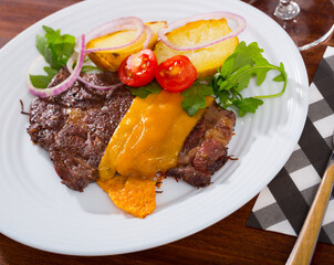 Well-done beef steak with baked potatoes and cheese served at plate with greens