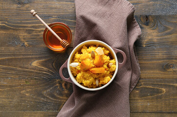 Pot of tasty millet porridge with pumpkin and honey on wooden background