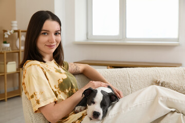 Beautiful young woman with cute staffordshire terrier puppy sitting on sofa at home