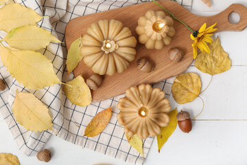 Beautiful composition with burning candles in shape of pumpkin and autumn leaves on white wooden...