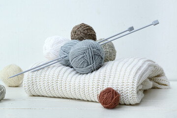 Knitted sweater, needles and yarn balls on white wooden table