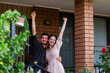 House key in hand of happy young homebuyer couple with arms out in delight