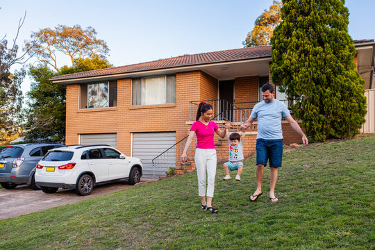 Family of three playing together on front lawn of home cars parked in driveway