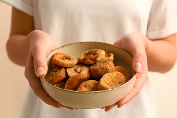 Woman holding bowl with tasty dried figs on beige background, closeup