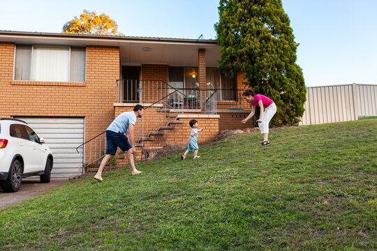 Australian family of three playing together on front lawn of home in evening