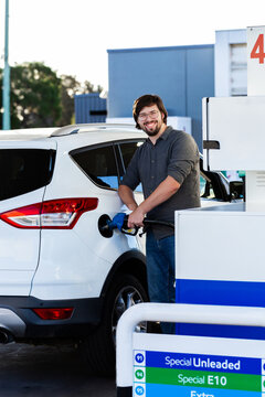 Happy young man in his twenties filling car with petrol at servo station