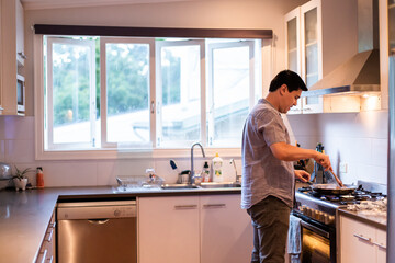 Man standing in the kitchen cooking food in a stovetop pan