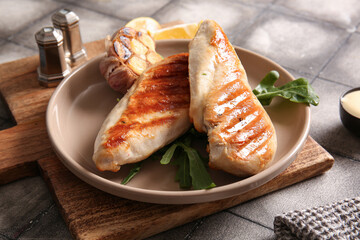 Plate of tasty grilled chicken breast with arugula and garlic on grey tile background