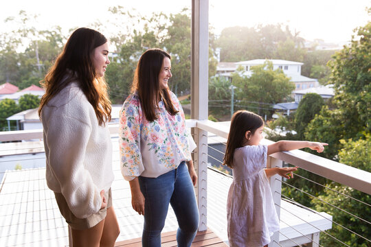 Mother and two daughters standing on the balcony happily looking across the street